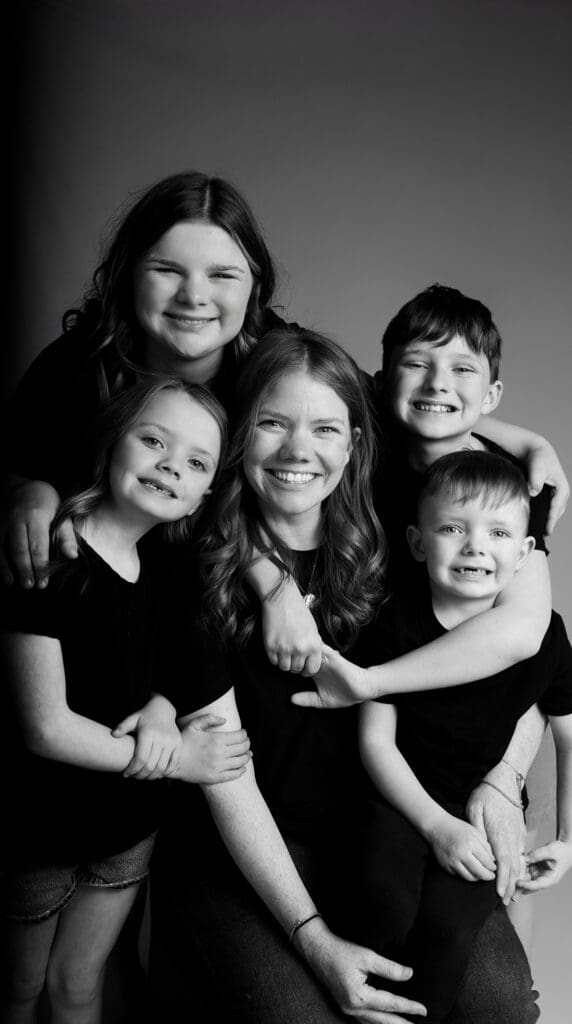 black and white portrait of mother with 4 children smiling and hugging her