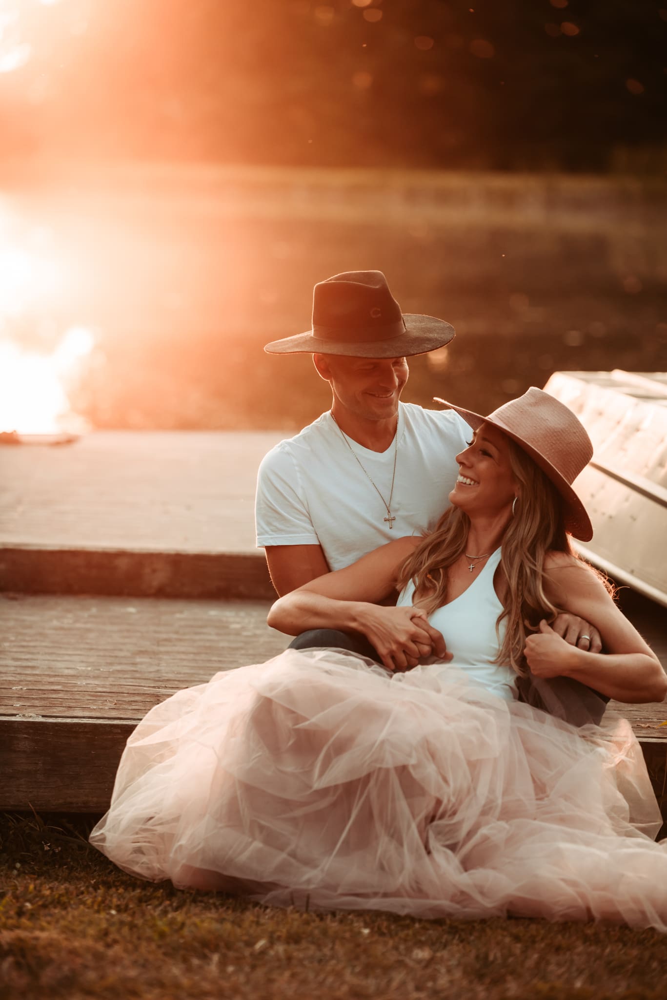 wife sitting in front of husband turning backwards to look at him smiling in the sunset