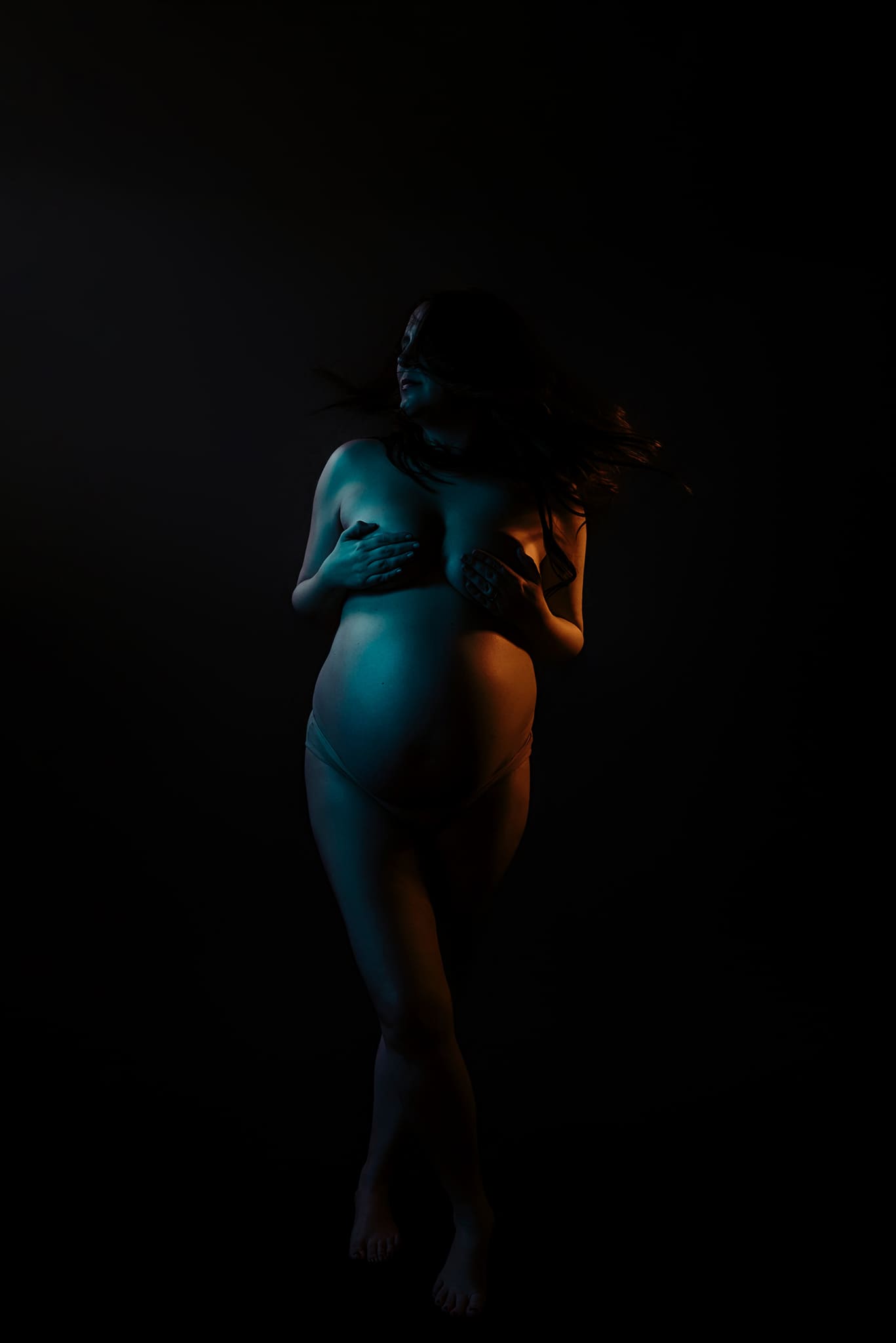 maternity mom side lit with blue and pink color showing the shape of her bump