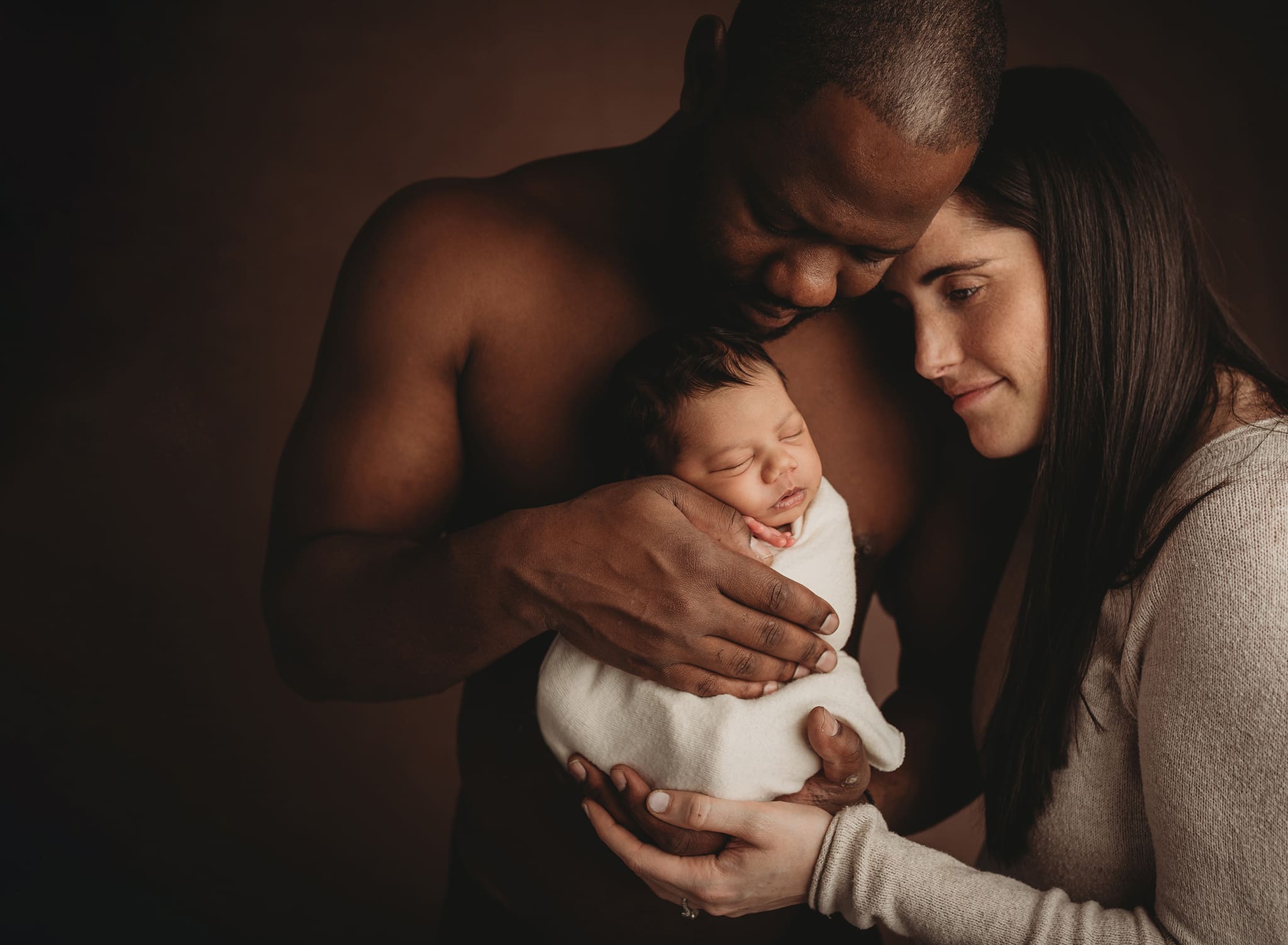 columbus ohio newborn photographer 25 couple in studio holding baby in front of dad and mom leaning head of dad chest staring at the baby