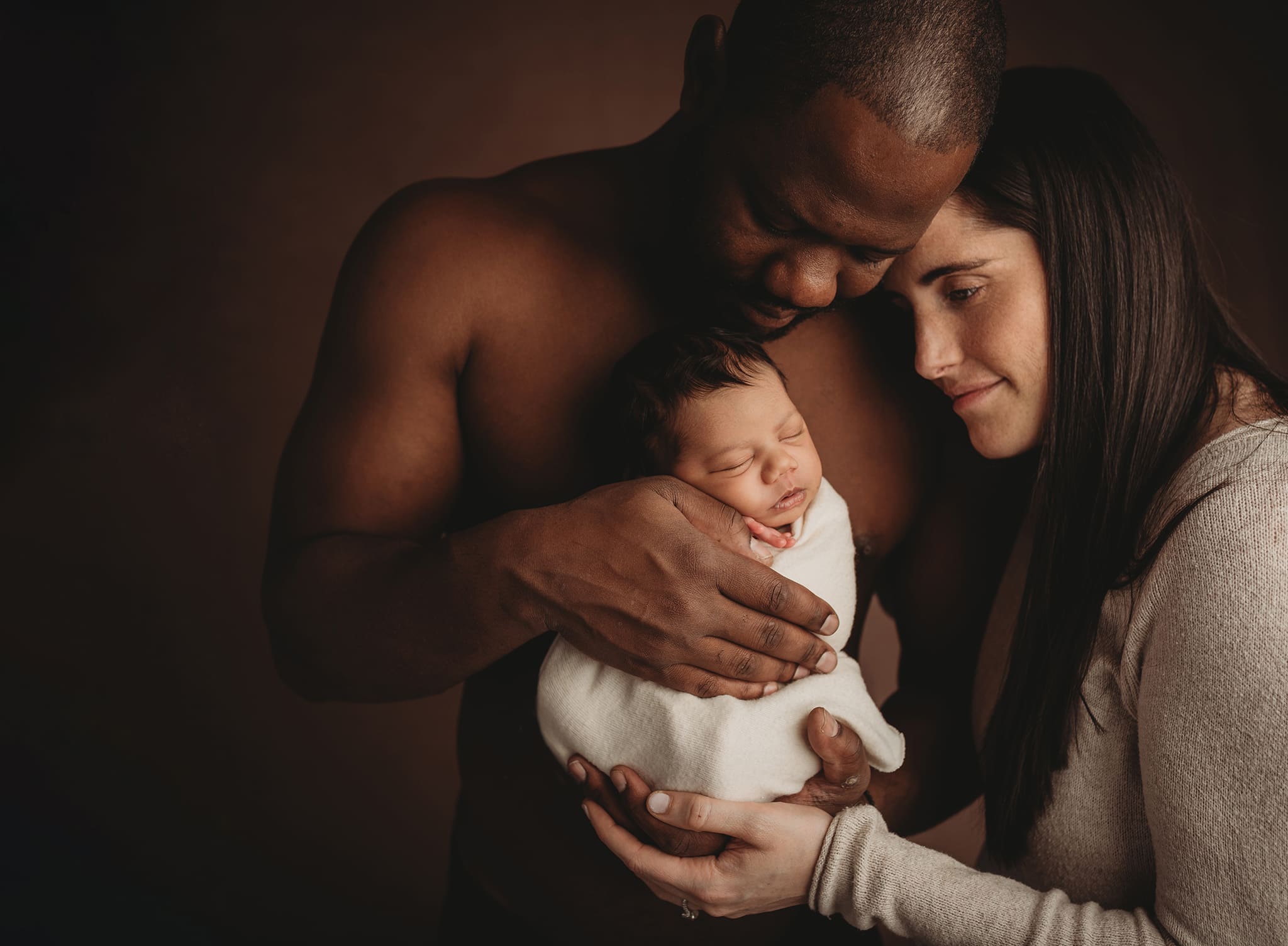 mom and dad snuggling newborn baby wrapped in ivory wrap skin to skin with dad