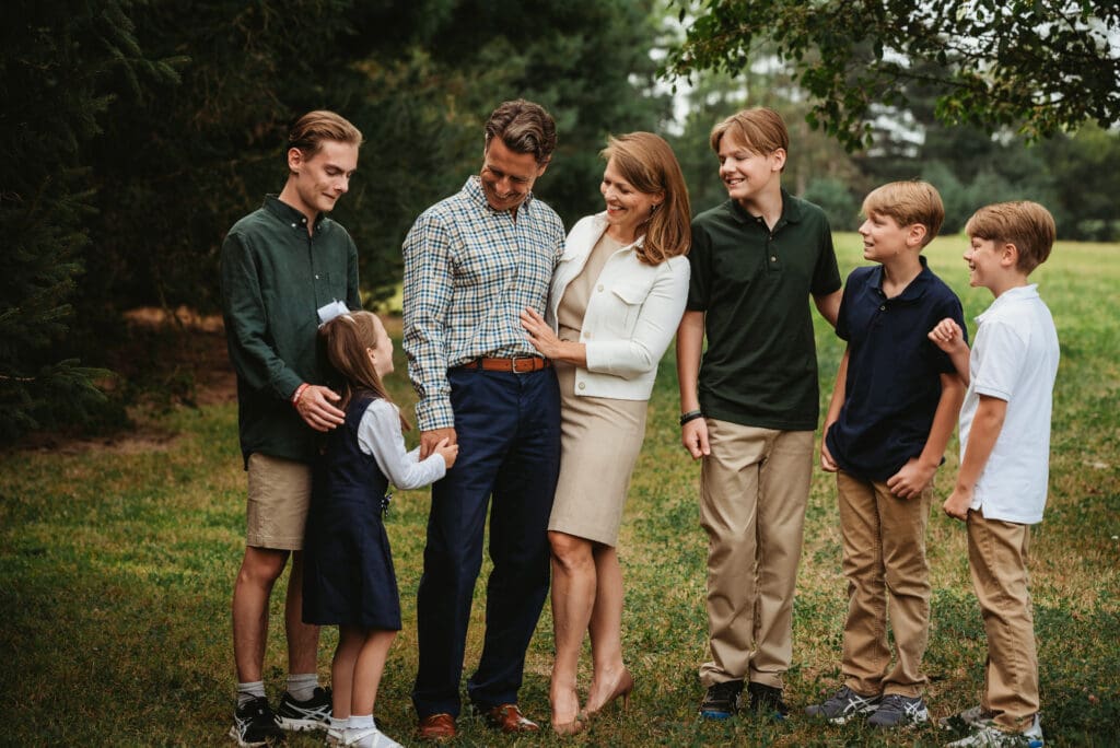 family of 7 posing outside in earth colors laughing at their sister and daughter