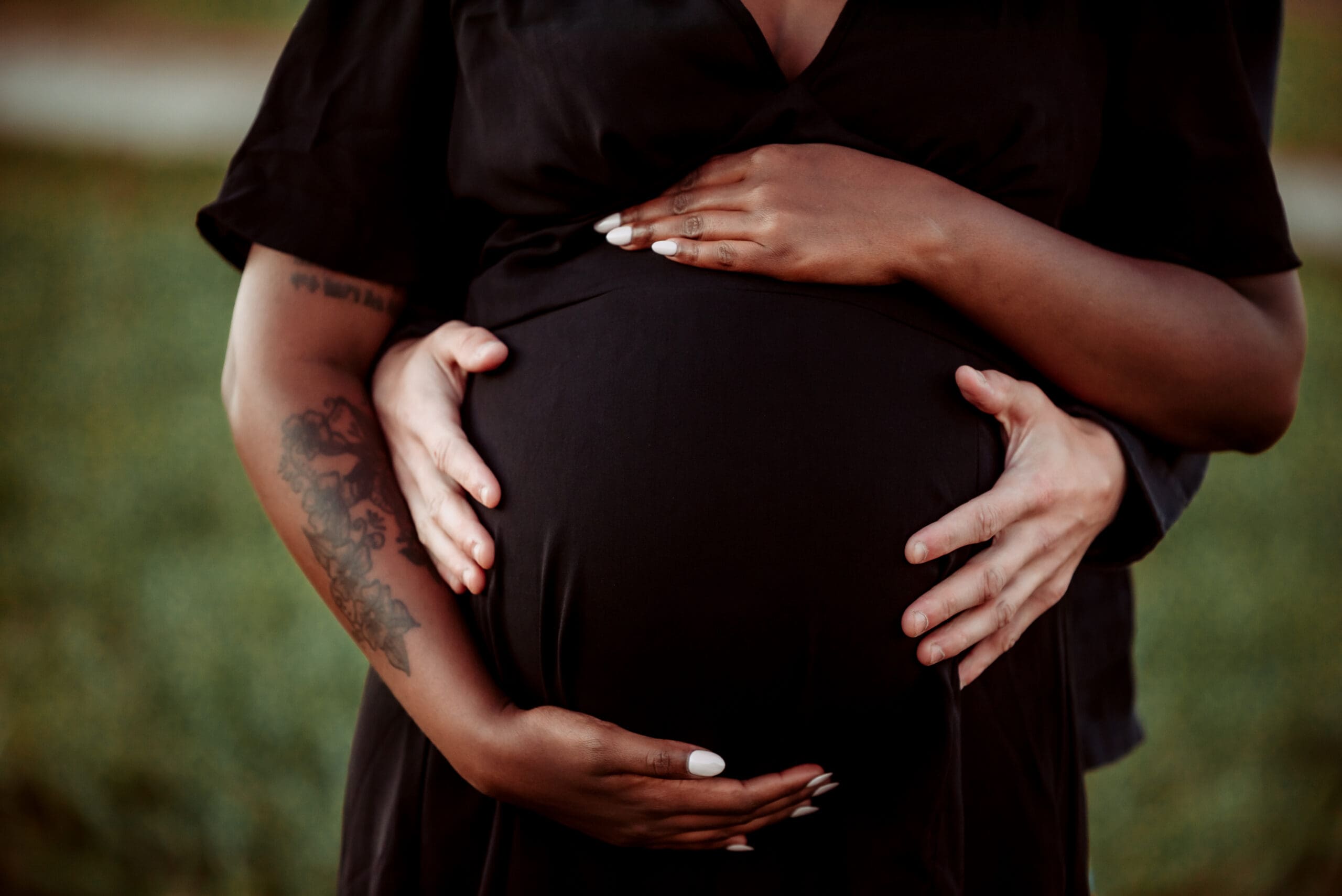 pregnant mom holding belly with father of baby holding belly from behind and only showing hands and belly