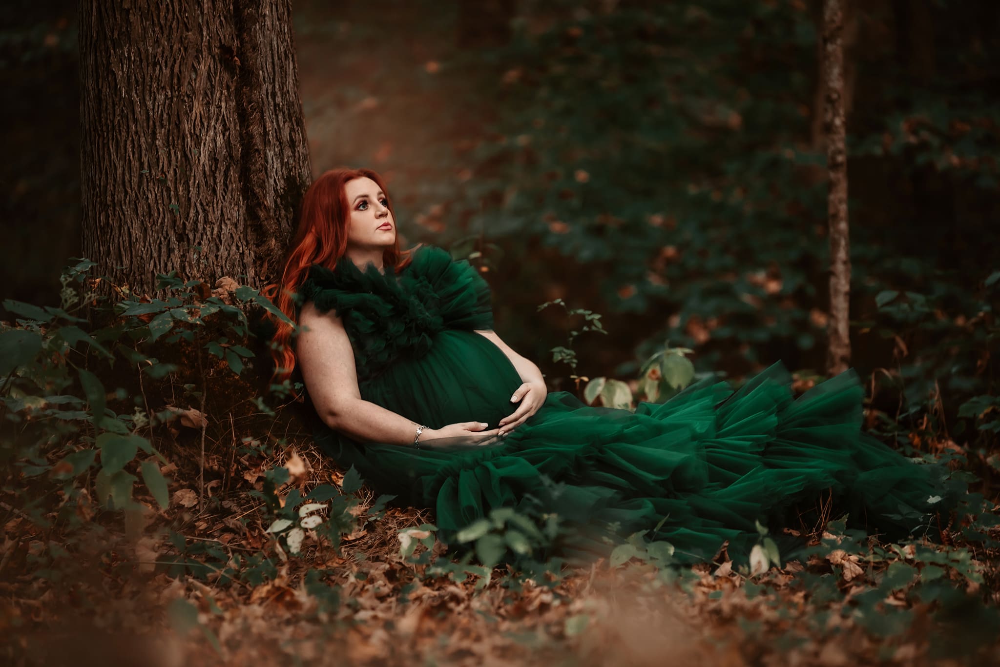 columbus ohio maternity photographer 19 forest maternity session pregnant woman in green gown sitting on ground leaning against the tree