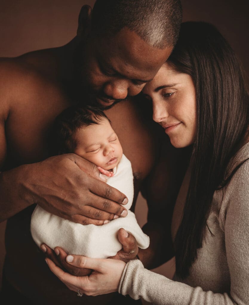 newborn baby girl being held by her dad and mom snuggled into his chest