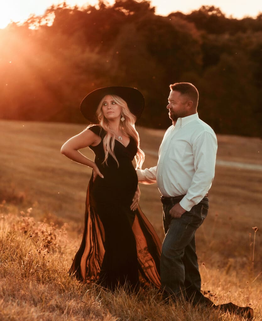 sunset maternity session with pregnant woman looking off and husand starting at her she is wearing a black dress