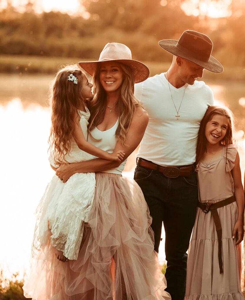 family of four at sunset laughing with each other by their family pond