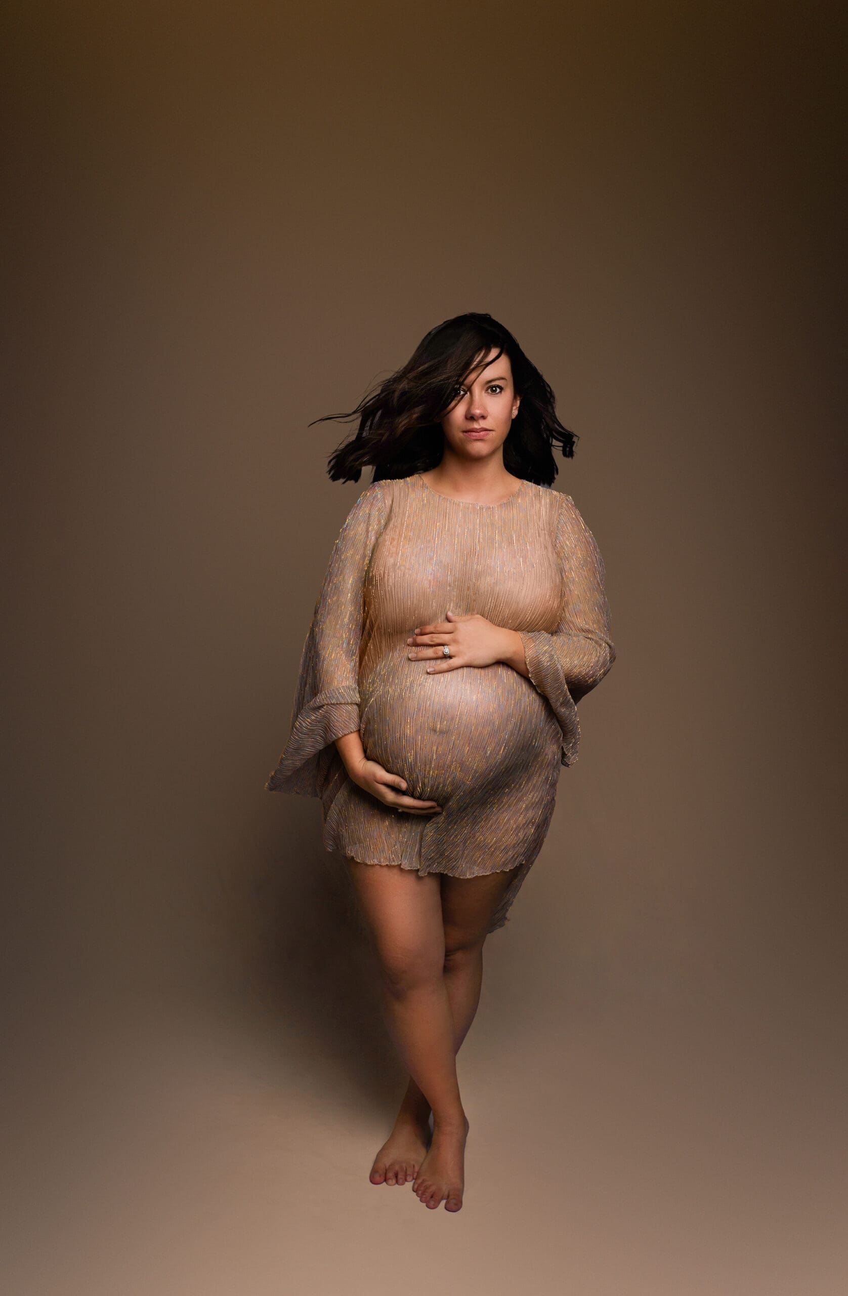 pregnant mother wearing a custom gown with sparkly fabric holding her belly looking serious
