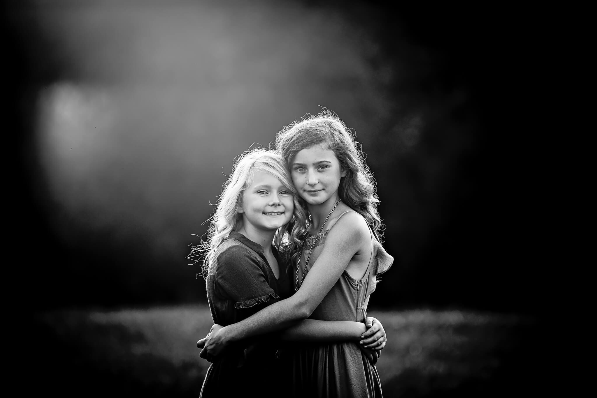 black and white images of sisters at sunset hugging