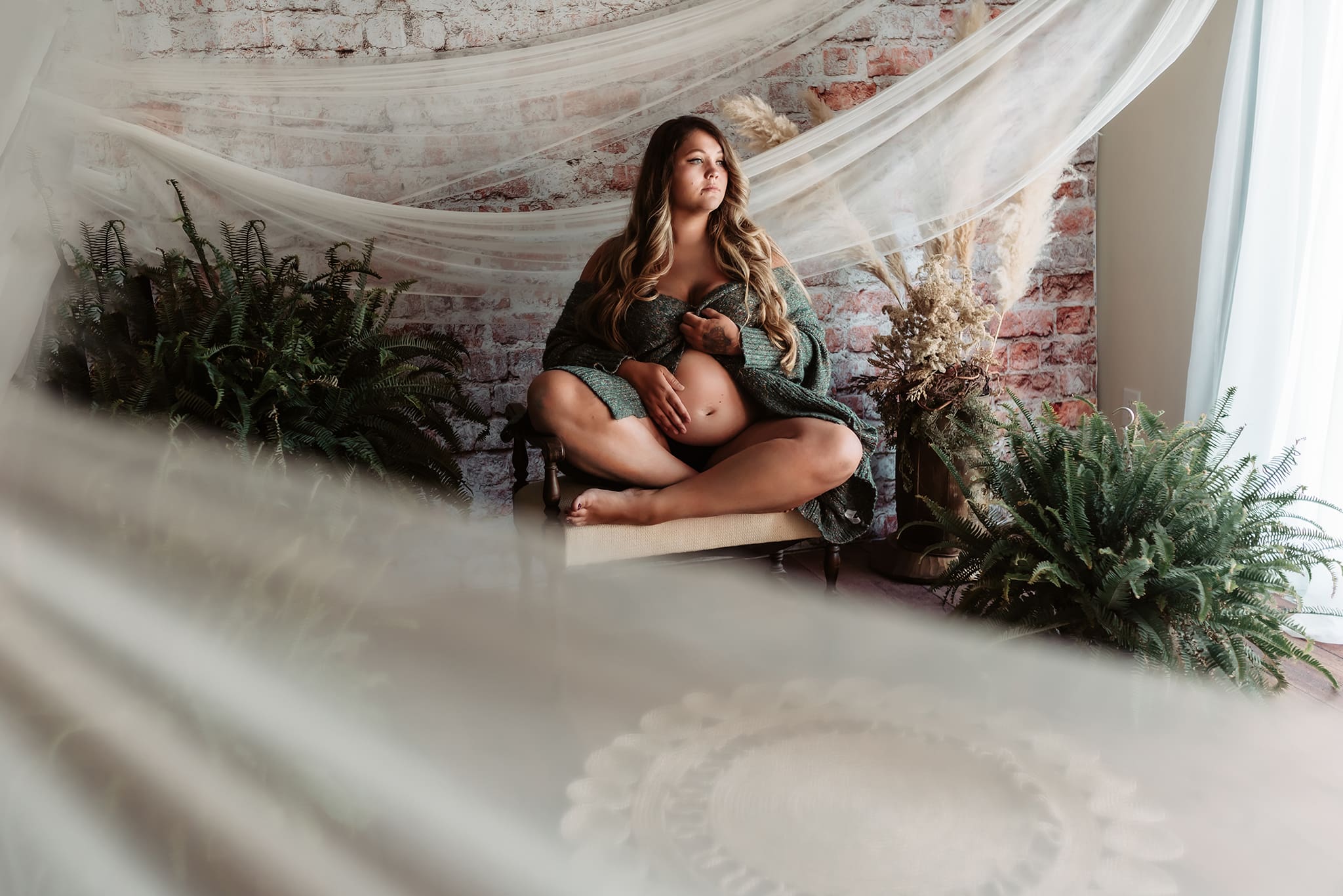 boho themed studio maternity session with mother sitting cross legged looking out the window