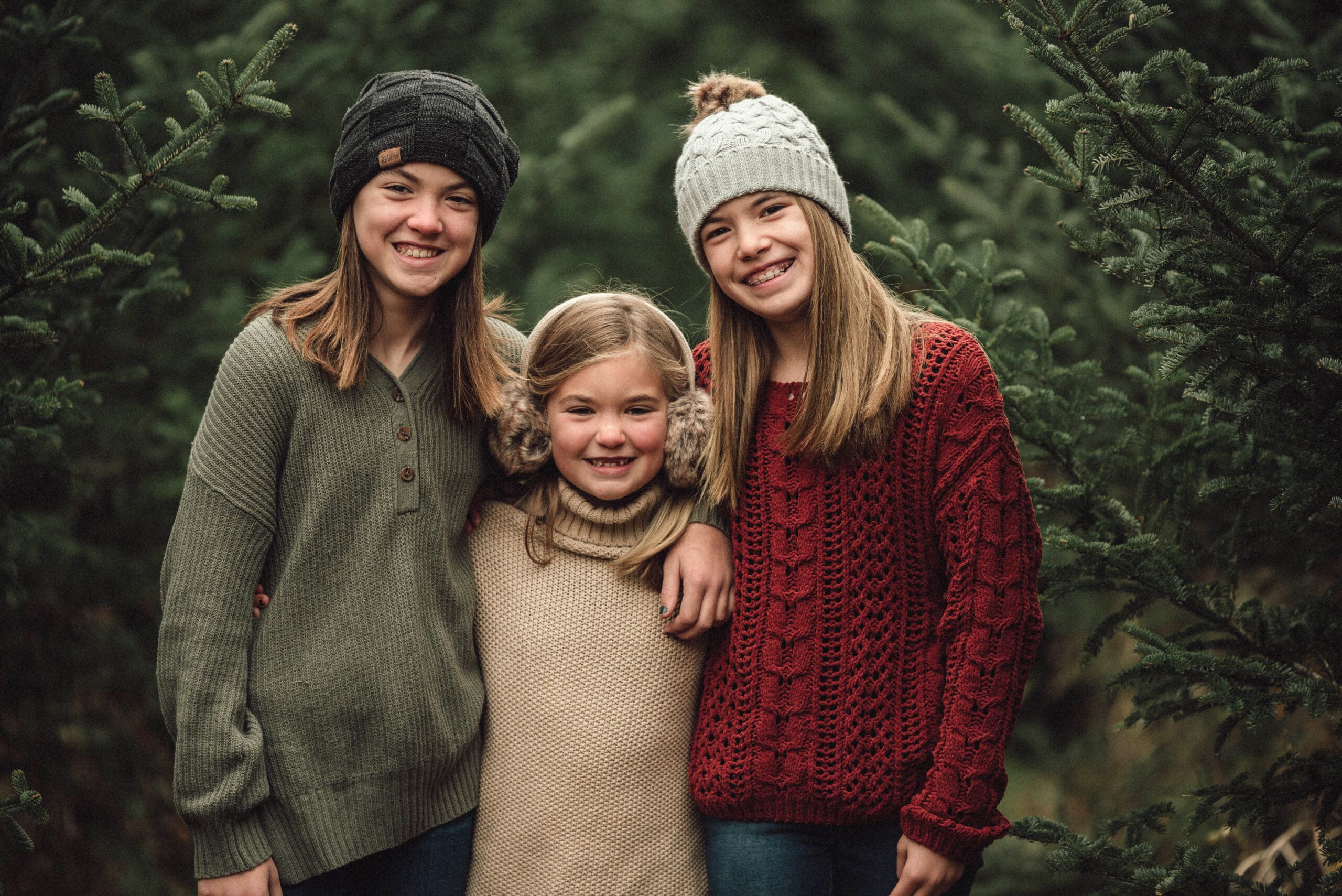 3 sisters standing in the christmas trees with hats on