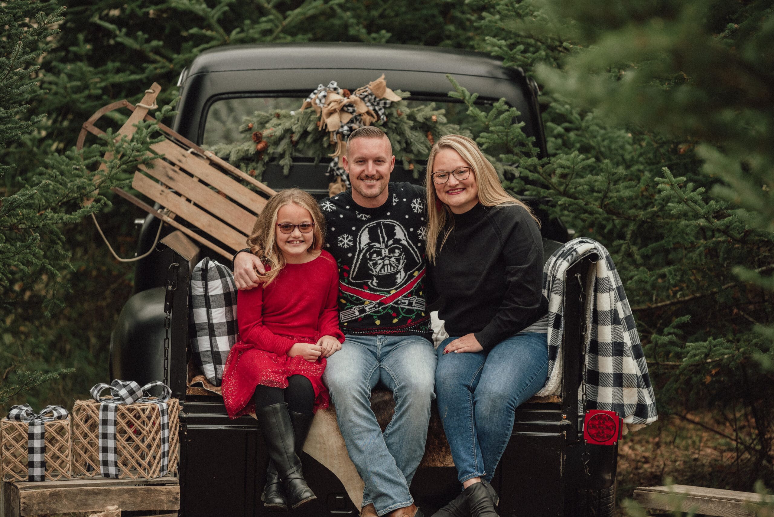 family of 3 sitting on the back of a old truck at a tree farm