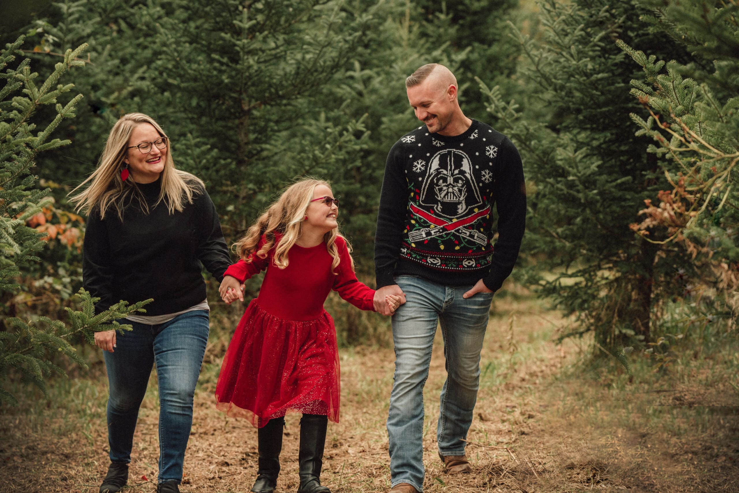family of 3 walking through the christmas trees laughing